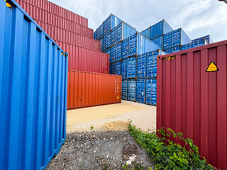 Fototapeta premium Stacked blue and red industrial shipping containers in a freight terminal.