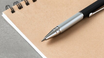 Fototapeta premium A silver black metal pen rests diagonally on a tan spiral notebook, ready to write.