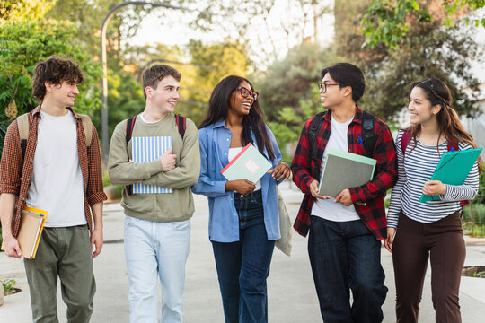 Multicultural students walking together talking holding notebooks outdoor park lifestyle