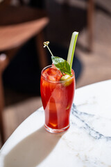 Red bloody mary cocktail with celery olive and ice served in tall glass on table in bar interior © Hihitetlin