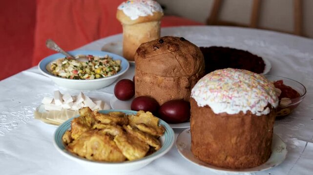 A festive Easter table with three paska breads, onion-dyed eggs, fried fish or patties, salads, cheese on white tablecloth. Traditional dishes create a rich holiday food spread cozy family atmosphere.