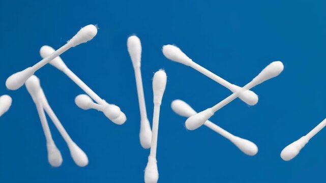 A clean, minimalist photo or 3D render of multiple white cotton buds scattered and floating in the air against a bright blue backdrop. Suitable for hygiene products, medical supplies, or cosmetic tool