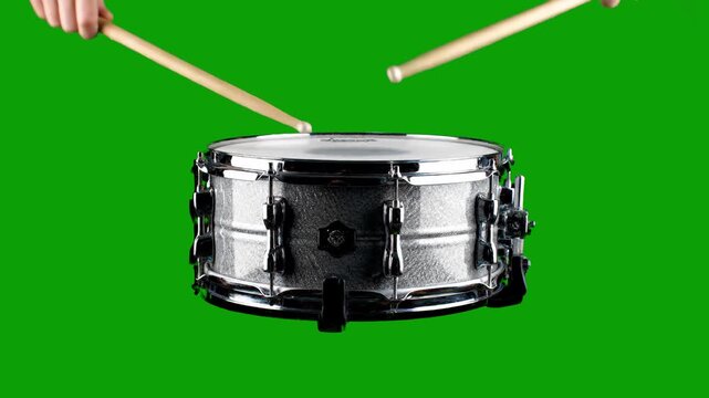 A close-up shot of a metallic snare drum being struck by drumsticks against a vibrant green screen background. This clip is ideal for music production, rhythmic