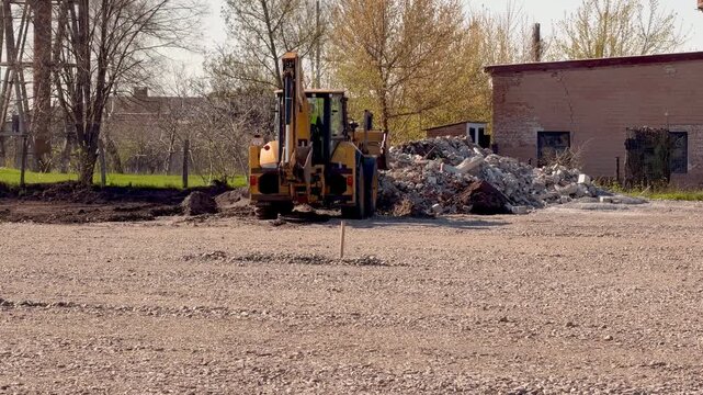 Yellow backhoe loader moving rubble on construction site