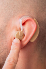 Fototapeta premium Closeup man wearing beige behind-the-ear hearing aid, modern medical device hearing loss compensation, audiology support, ear health and deafness, Medical tech solution improve auditory perception