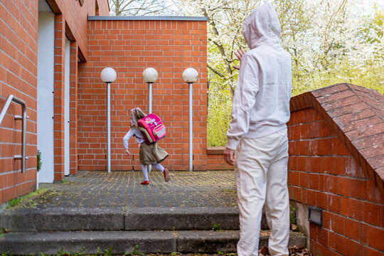 man in white suit watching young girl school entrance from distance, attention urban setting, stranger danger, child safety awareness, potential risk situation, vigilance and protection public spaces