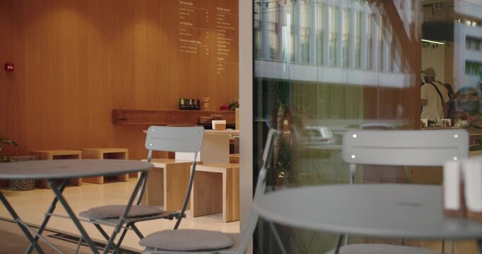 A stylish coffee shop interior reflecting modern minimalistic design. The scene includes wooden walls, a clear glass facade, and contemporary furniture with a serene ambience.
