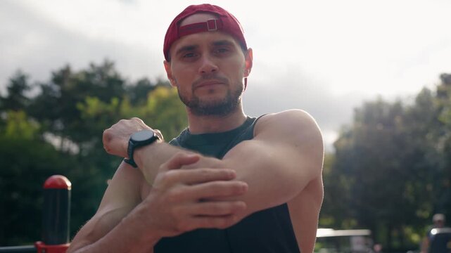 Young athletic man warming up before outdoor workout. Fitness male stretching arms and looking at camera. Sportsman preparing for exercising outside. Motivation for active lifestyle.