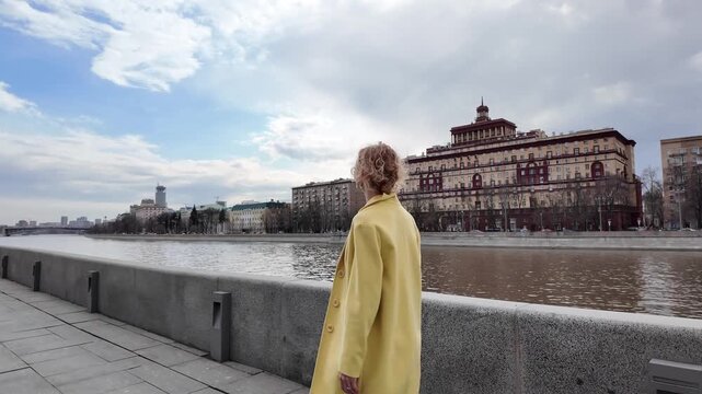 Woman in yellow coat walking along granite embankment near Moscow River with building background