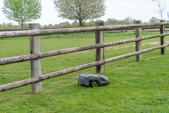 Charencey, France - 04 12 2026: A robotic lawnmower automatically mows the lawns of a country house, with trees, fields, flowers and wooden barriers in Le Perche countryside