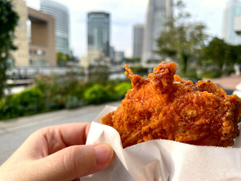 フライドチキン ─ 手持ちの骨付きチキン・都市背景の屋外