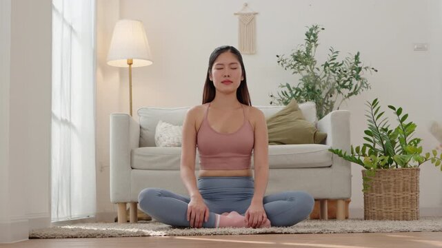 Beautiful Asian woman meditating in lotus pose at home