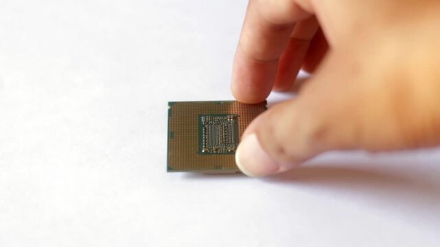 Close up of a hand holding a modern computer CPU processor chip against a white background. Concept for hardware technology, PC building, and digital processing.