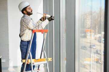 Construction worker sealing window frame on ladder © Serhii