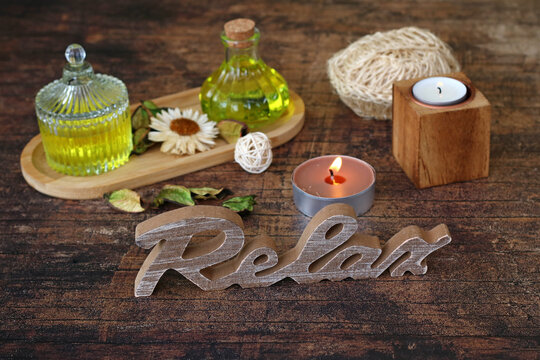 Wellness-Stillleben zur Entspannung: Schriftzug 'Relax' mit Aroma&ouml;len und Kerzenschein auf rustikalem Holz.&ldquo;