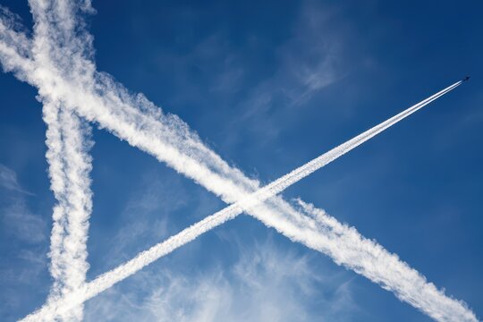 Airplane contrails form a striking X shape against a clear blue sky with wispy clouds.
