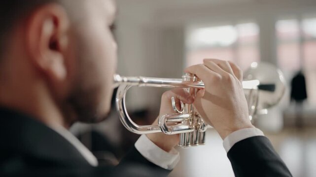 A young and handsome man dressed in a suit plays the trumpet with desire and inspiration. A male jazz singer plays the trumpet on a white background in a modern studio. Music room.