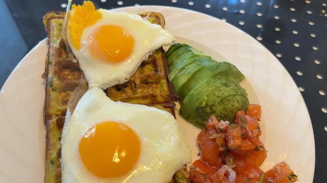 Savory waffle breakfast with fried eggs, avocado, and salsa on a white plate background