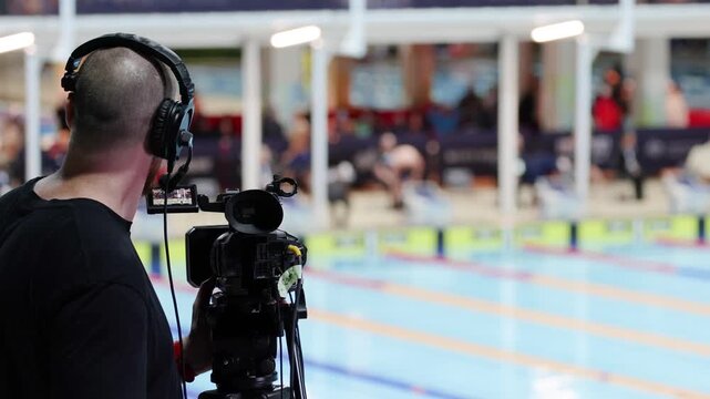 Camera operator filming professional swim competition, capturing dynamic footage of swimmers in action, broadcasting live event.