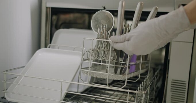 Woman hand in glove put manicure tools in disinfector washer for cleaning and sterilization. Manicurist assistant prepare and disinfect manicure tools at sterilization room with medical equipment.