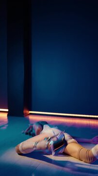 Professional female dancer moving with passion and grace, performing a sensual floorwork routine in high heels inside a studio with colorful neon lights and a dark, moody atmosphere. Vertical