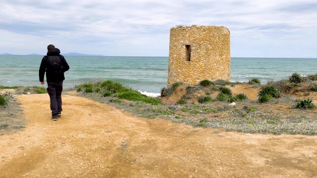 Rear view of a photographer walking along a coastal path heading towards a watchtower in a natural landscape
