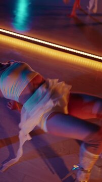 Passionate blonde woman in high heels performing a sensual modern dance choreography on the floor of a studio with neon lights, showcasing flexibility, grace, and contemporary art. Vertical