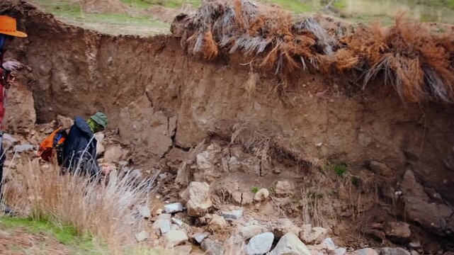 two hikers descending into deep eroded ravine during mountain trek, showing risky decision, navigation challenge and potential danger in rugged and unstable natural environment, risky mountain route