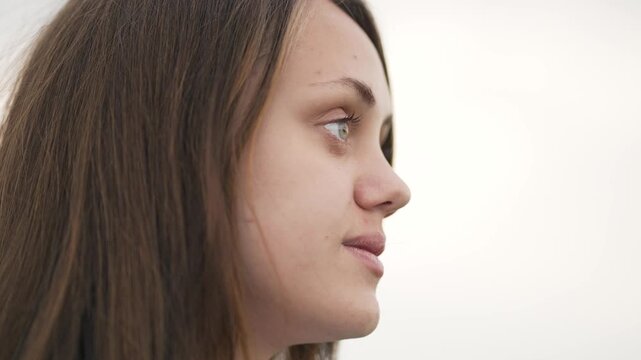 Young woman looking to side in soft pale sky setting, profile portrait showing face and hair, young expression with thoughtful gaze and beauty, calm pose with skin detail and natural tone soft light