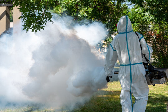 Rear view of an exterminator in a white chemical protection suit using a machine outdoors.