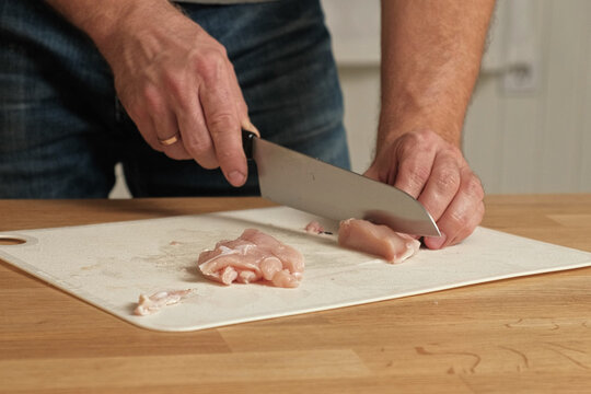 Man butcher cut raw meat with sharp knife at home kitchen. Male person cutting the chicken fillet pieces for cooking. Preparing chopping food. Split poultry breast. Healthy lean meat, low cholesterol