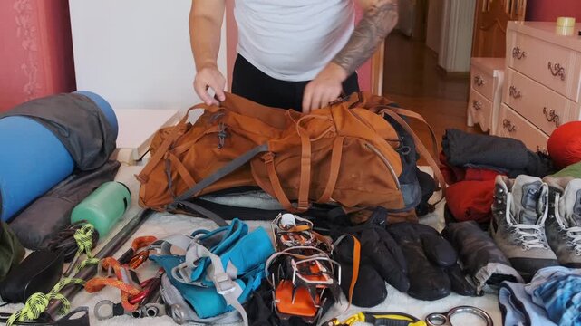 male hands packing backpack with mountaineering and hiking equipment at home, organizing professional gear for outdoor trip, preparation process showing travel planning and adventure setup