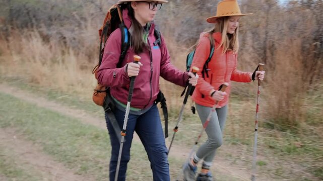 two women walking side view trail with backpacks and trekking poles near mountain lake, enjoying active travel together, outdoor hiking activity, connection, freedom and exploration in nature