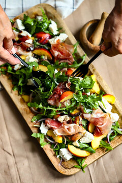 Arugula salad with peach and prosciutto on a wooden board