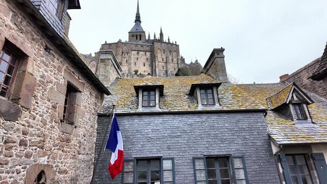 Low angle static shot of the Mont Saint-Michel Abbey towering over traditional stone and slate houses..