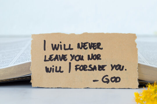 I will never leave you nor will I forsake you-God, handwritten quote with holy bible book and white background. Christian biblical concept. Copy space.