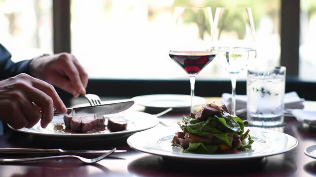 Elegant hands, ECU video, dining gourmet food with silver cutlery on table. Wine glasses, cinematic light, bokeh, concept of luxurious fine dining.