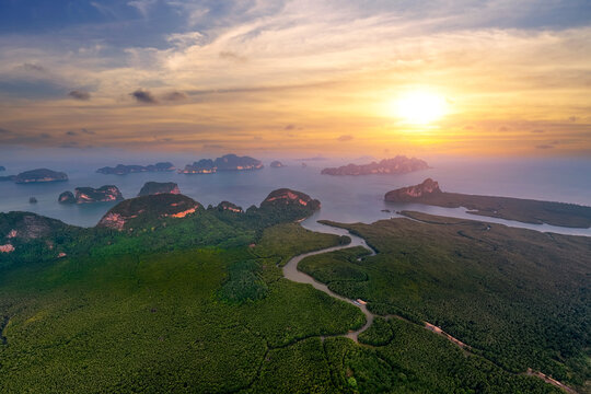 Aerial view majestic limestone formations rise above emerald waters fringed by winding mangroves, with a bustling coastal village visible at sunrise.