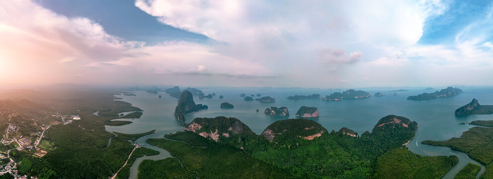 A panoramic aerial view from above shows majestic karst formations rising above emerald waters around verdant forest jungles fringed by winding mangroves.