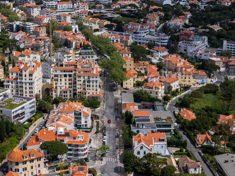 Aerial view of Monte Estoril featuring orange-roofed residential buildings, lush green trees, and a red car on a quiet street in Estoril, Lisbon, Portugal.