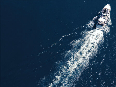 Aerial view of a luxury yacht cruising through deep blue water leaving a long white wake.