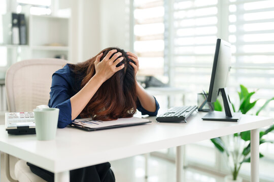 Burnout at Desk: A woman, overwhelmed by stress, sits at her desk, hands clasped to her head. The image is a stark portrayal of work-related pressure.