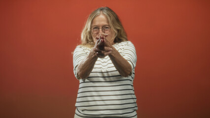 Senior blonde woman in striped shirt with hands clasped pointing forward in studio; steadfast...