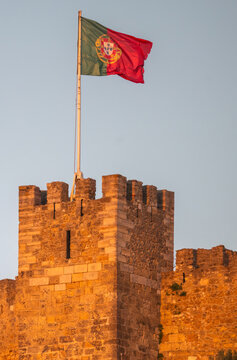 Aerial view of the Portuguese flag waving atop a stone tower of Sao Jorge Castle during golden hour in Lisbon, Lisbon, Portugal.