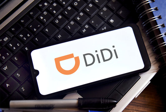 DiDi logo on a smartphone screen with a laptop in the background. DiDi Chuxing is a Chinese technology and transportation giant (similar to Uber).