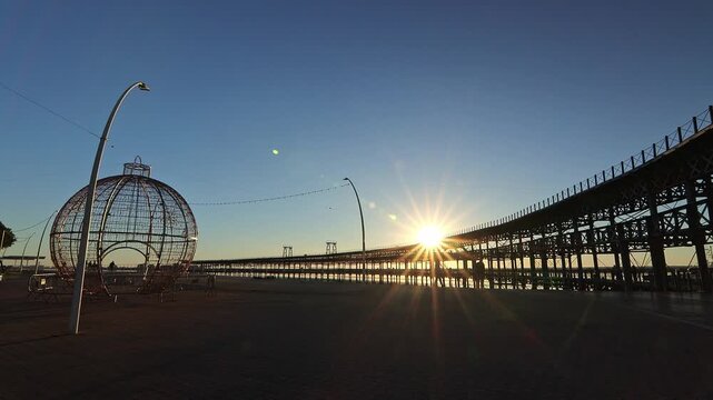 Stunning golden hour sunstar over the historic iron Rio Tinto Pier. Silhouette of a large Christmas ornament on the promenade. Huelva, Andalusia, Spain.