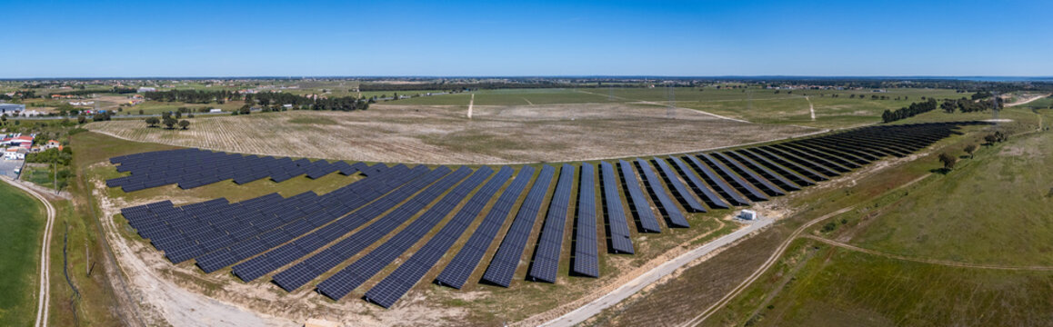 Aerial view of a large solar farm with rows of photovoltaic panels across green fields under a clear blue sky in Palmela, Setubal, Portugal.