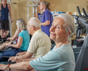 Obraz premium Group of senior adults using rowing machine with coach at gym