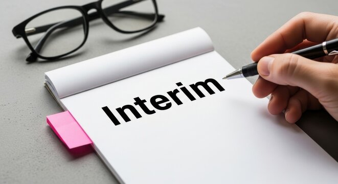 Interim text on white notepad, hand holding pen writing interim word, business management and temporary employment concept, office desk with glasses