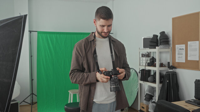 Man holding a dslr camera, checking settings and occasionally raising it to his eye in studio; focused creativity.
